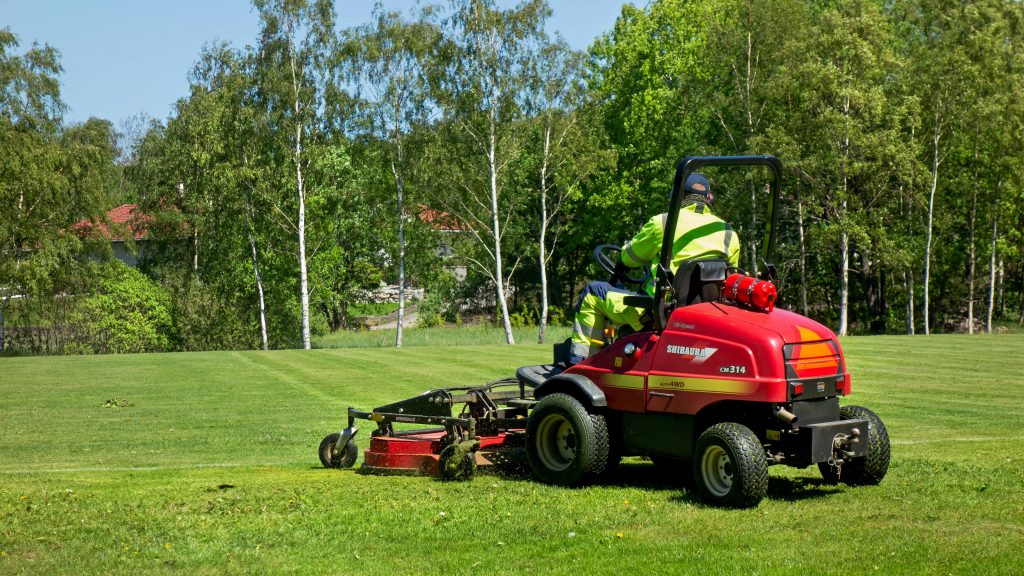 Man mowing a sport field with a ride-on lawn mower.