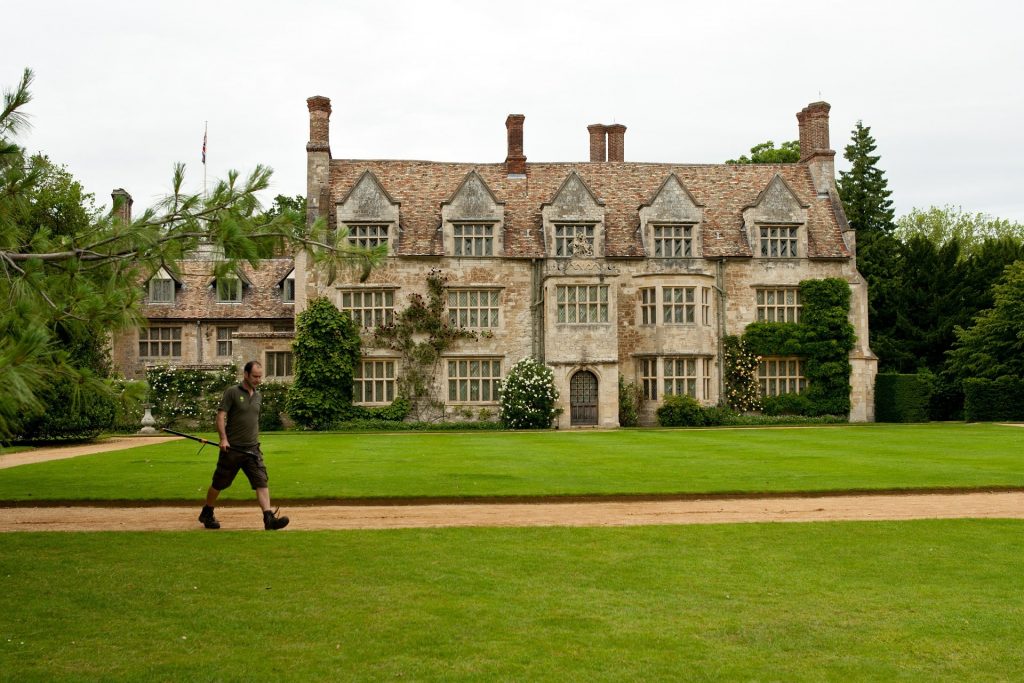 Man walking with a strimmer by a large house.