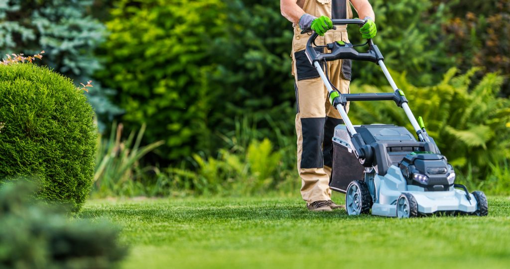 Man using a cordless electric lawn mower.